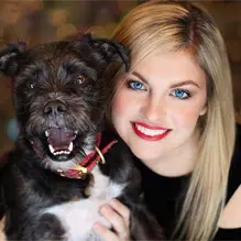 A smiling blonde woman holding a happy black dog with a red collar